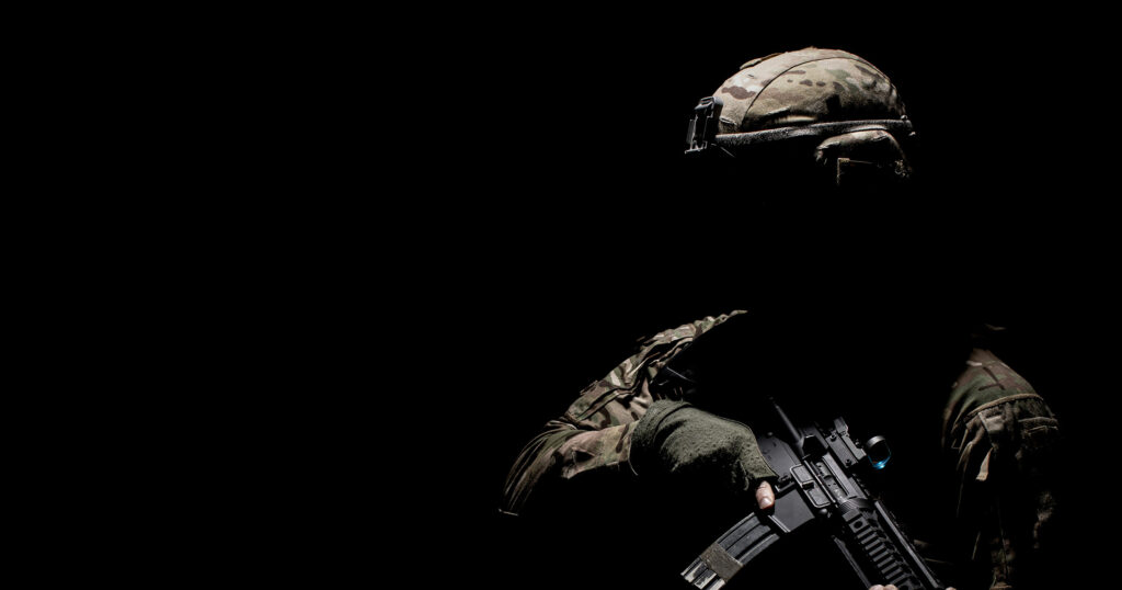 Soldier on a night operation holding a rifle in low-light conditions.