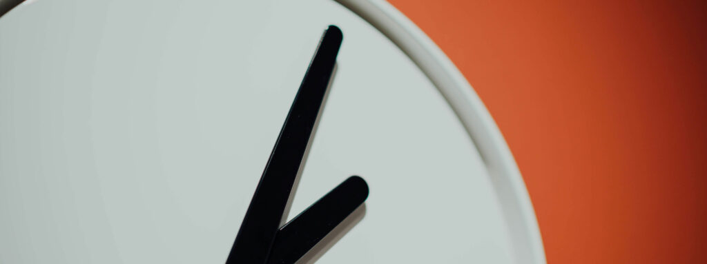 Time constraints shown by a large clock in front of an orange wall